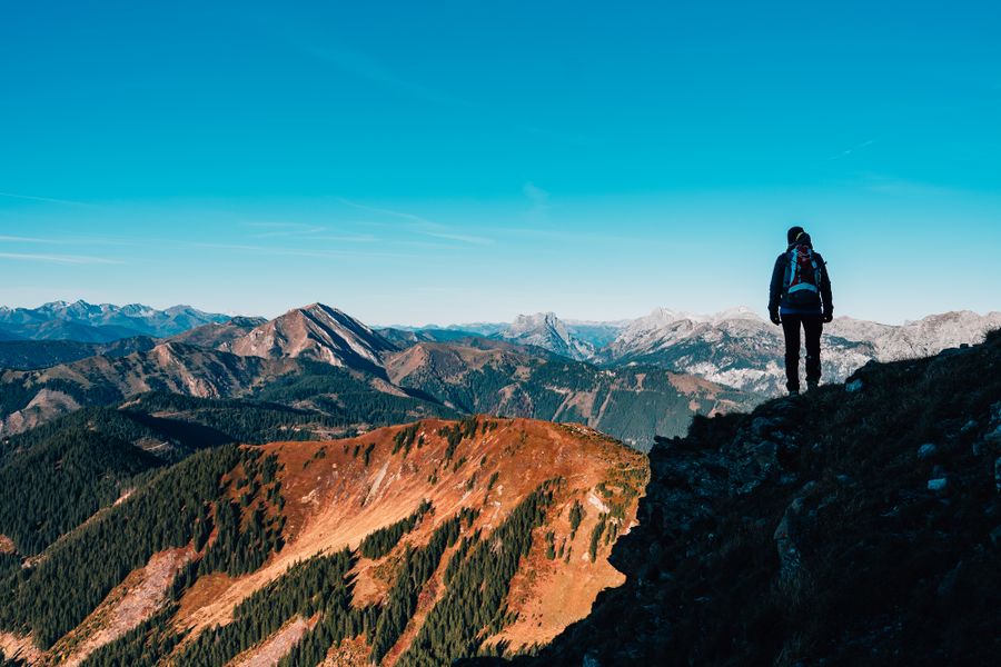 man in black jacket standing on rock formation under blue sky