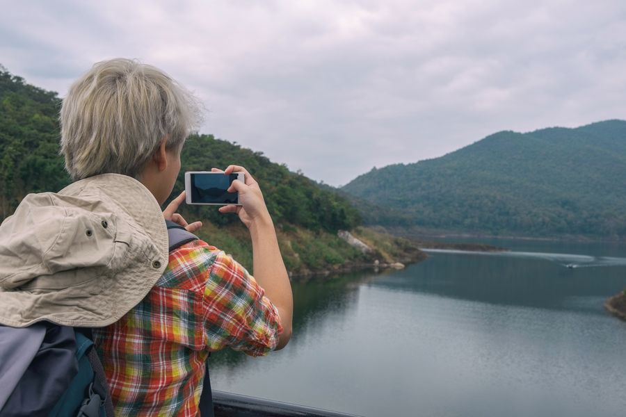 Person photographing a beautiful mountain lake view with a smartphone, enjoying outdoor adventure. — Developers · Bhutan: Hiking the ridge: trail map offline, emergency numbers saved.