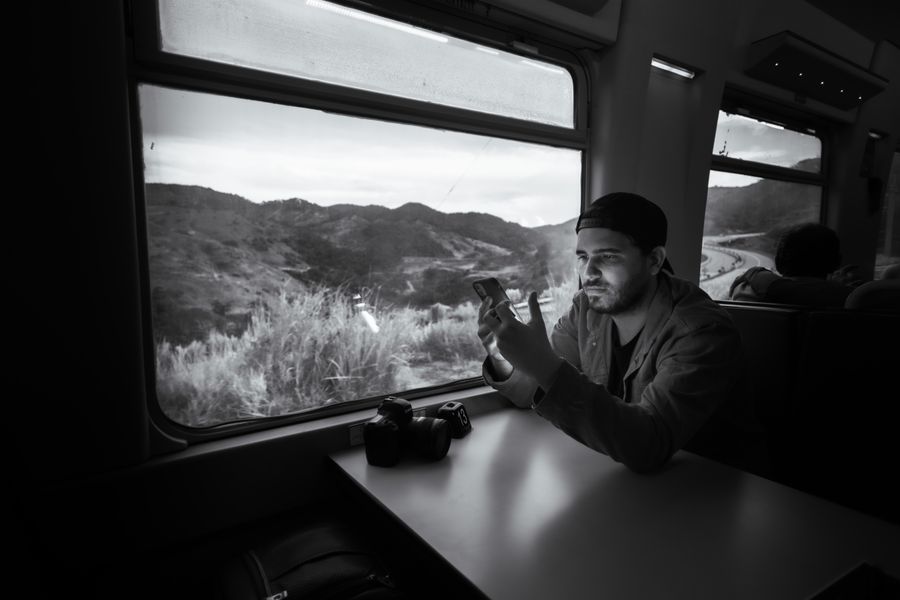 Man using a smartphone on a train journey through scenic landscape. — Developers · Sudan: The modern arrival: online before the seatbelt sign goes off.