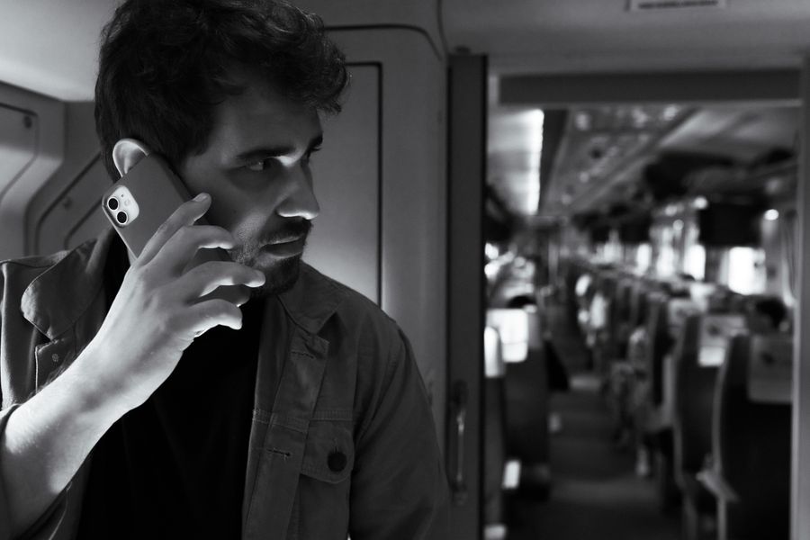 Black and white photo of a man using a smartphone while traveling on a modern train. — Developers · Sudan: Café office: hotspot running, video call stable, no hotel Wi-Fi roulette.
