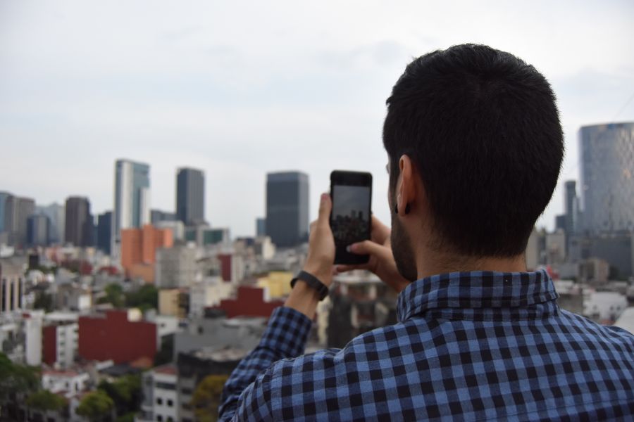 Man photographing urban cityscape with smartphone against skyline. — Developers · Lesotho: The viewpoint at golden hour: livestream the sunset to everyone back home.