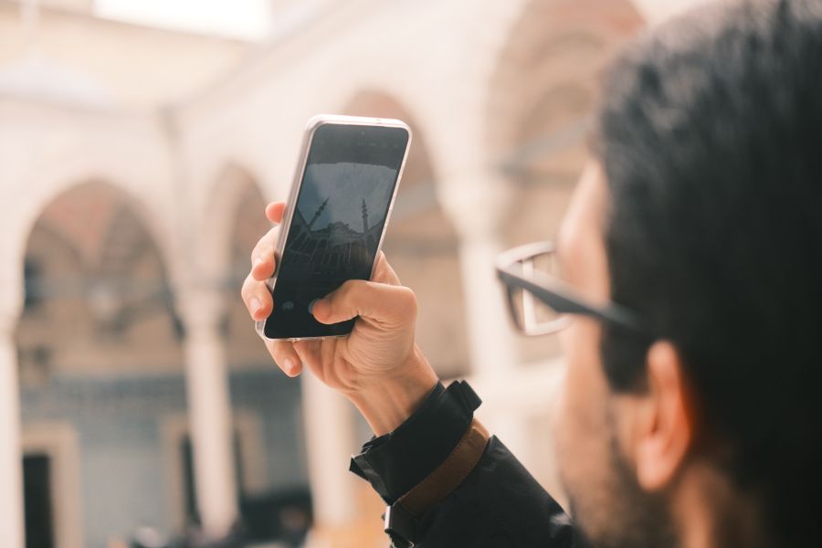 An adult male photographs a mosque using a smartphone outdoors with a focus on capturing architecture. — Developers · Senegal: The food tour: every recommendation looked up on the spot.
