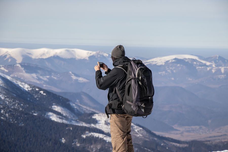 A person capturing the stunning view of snowy mountains with a smartphone. — Developers · Russia: Rainy-day backup plan: indoor attractions researched from the hostel bunk.
