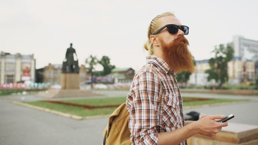 Hipster with a beard and sunglasses in a city square holding a smartphone. — Developers · Cuba: Currency exchange, skipped: the phone pays at the real rate.