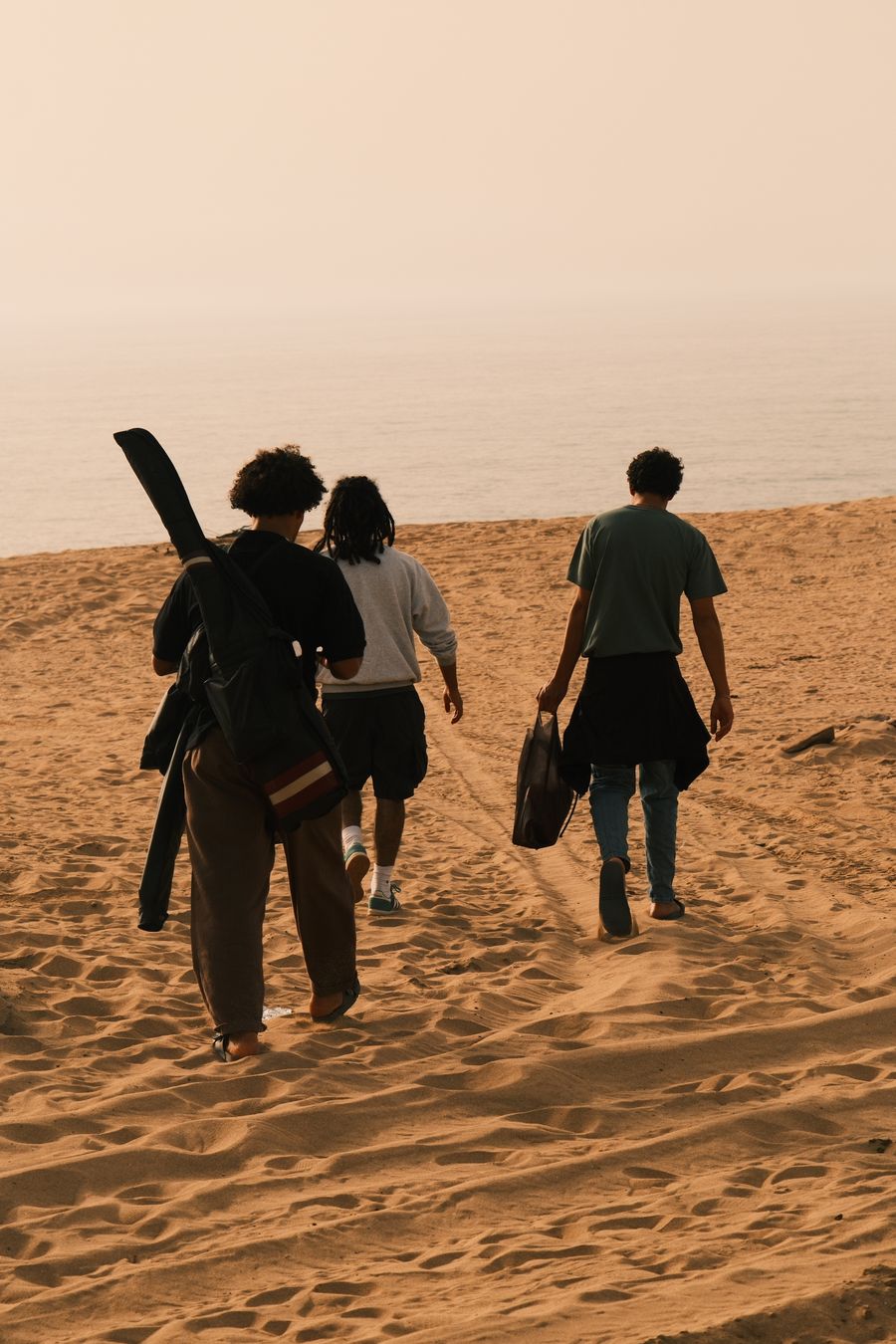 three friends walking on a sandy beach at sunset