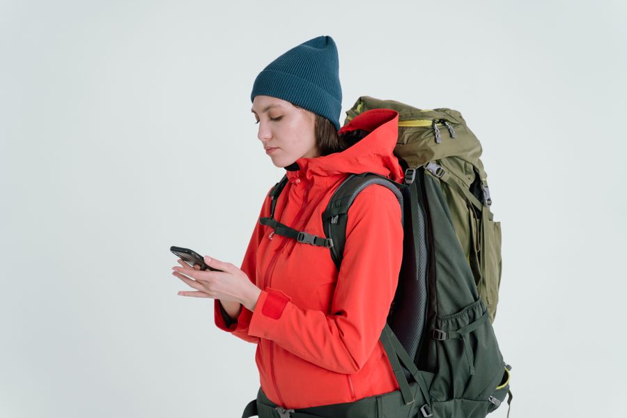 A woman in outdoor gear checking her smartphone, ready for adventure.